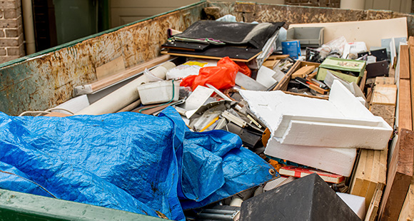 a skip full of waste to be taken away by a waste disposal team